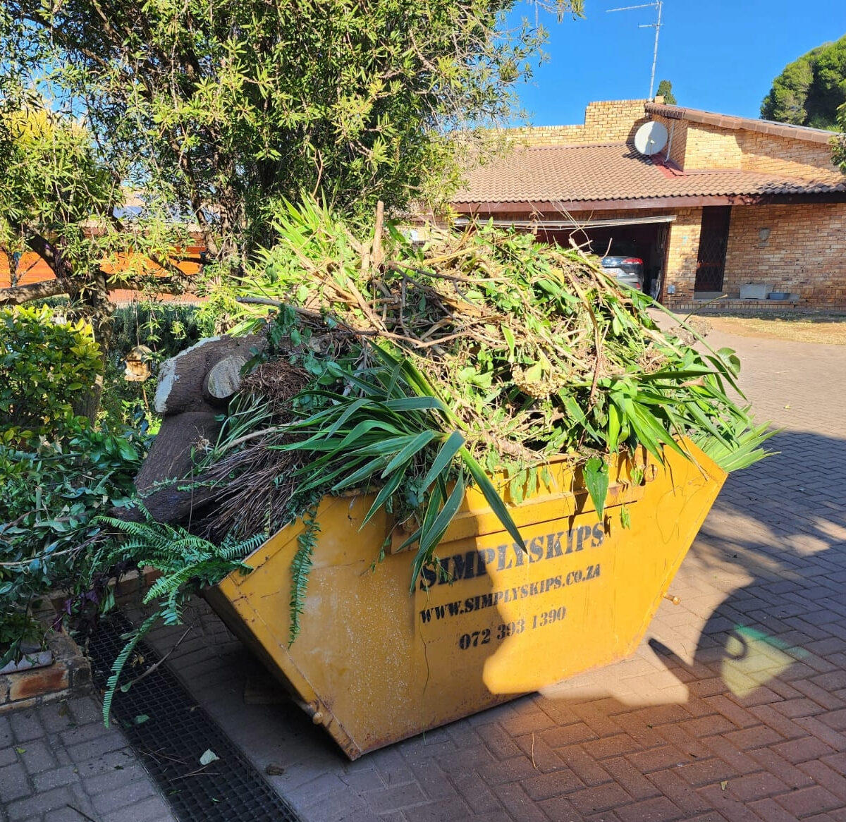 Yellow SimplySkips mini skip bin filled with garden refuse in a Roodepoort driveway
